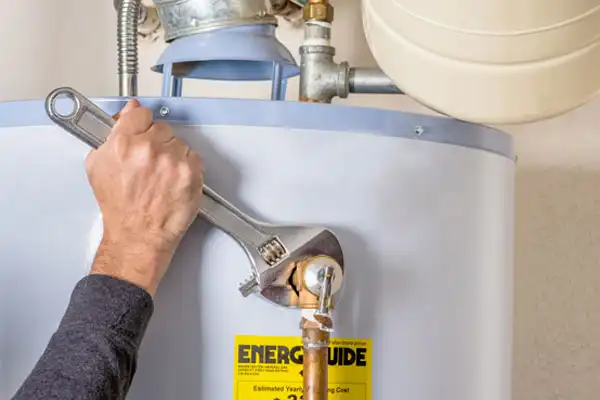 Person using a wrench to tighten a fitting on a water heater, with an "EnerGuide" label visible.
